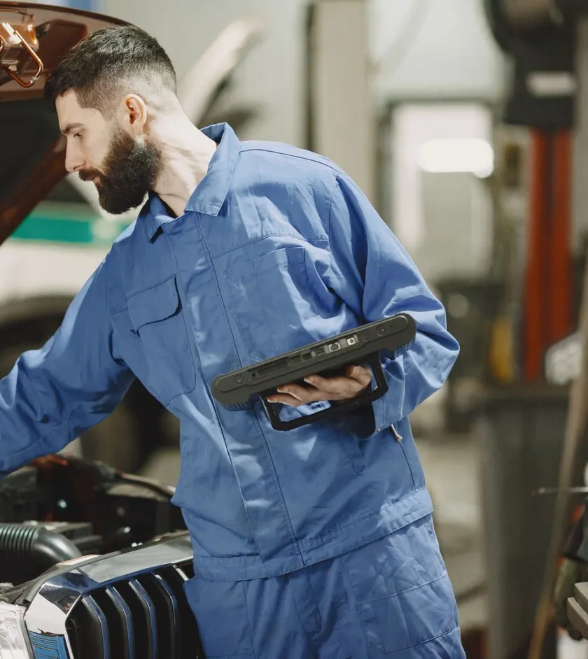 Mechanic in blue coveralls checking an engine with a tablet