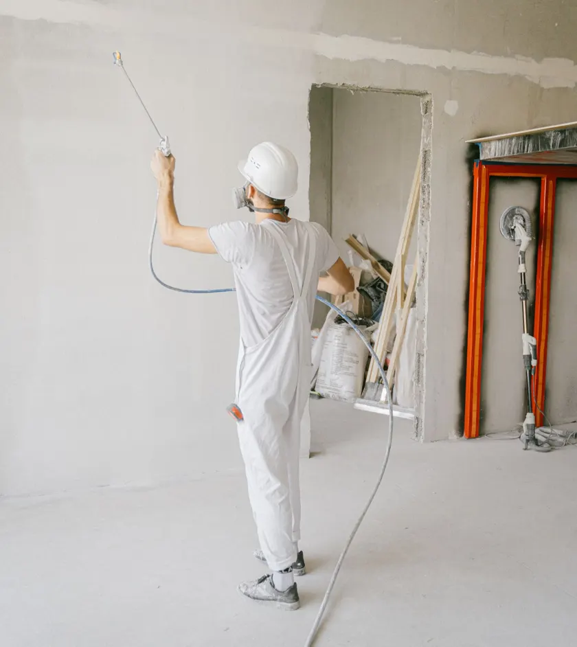 Construction worker spraying paint inside a building under renovation