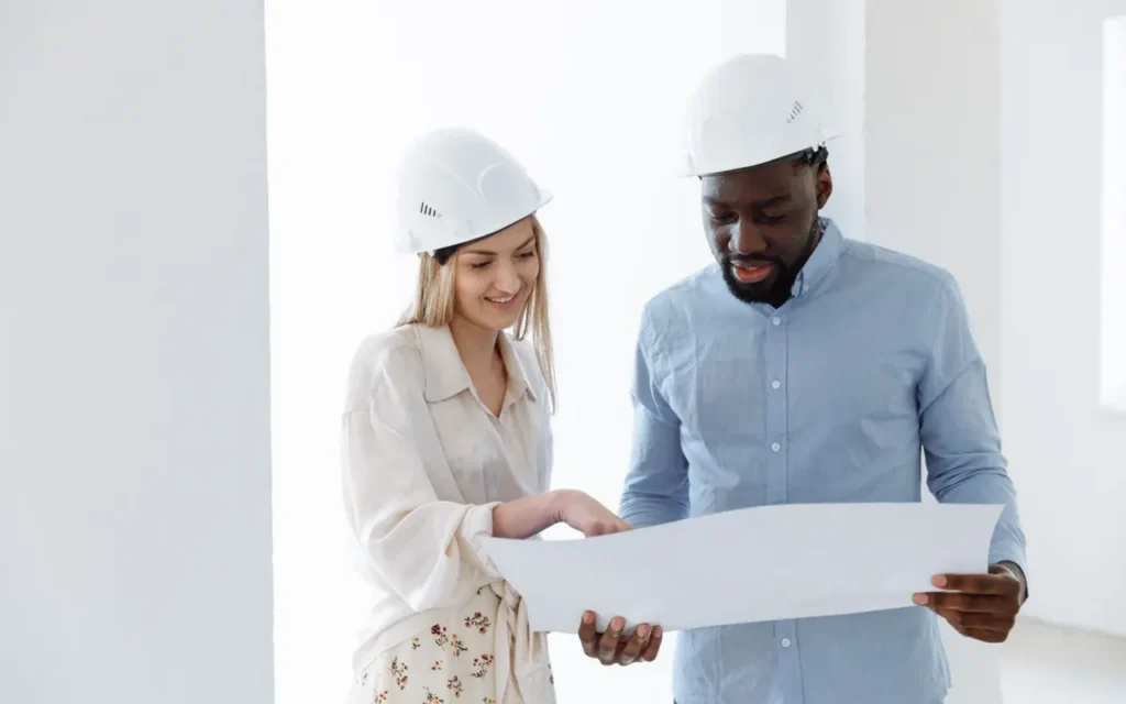 Contractor and client in hard hats reviewing a blueprint together