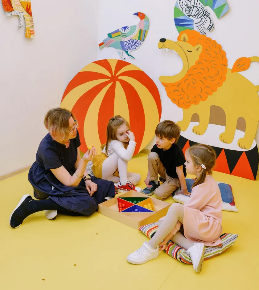 Teacher playing a learning game with young children on a colorful classroom floor