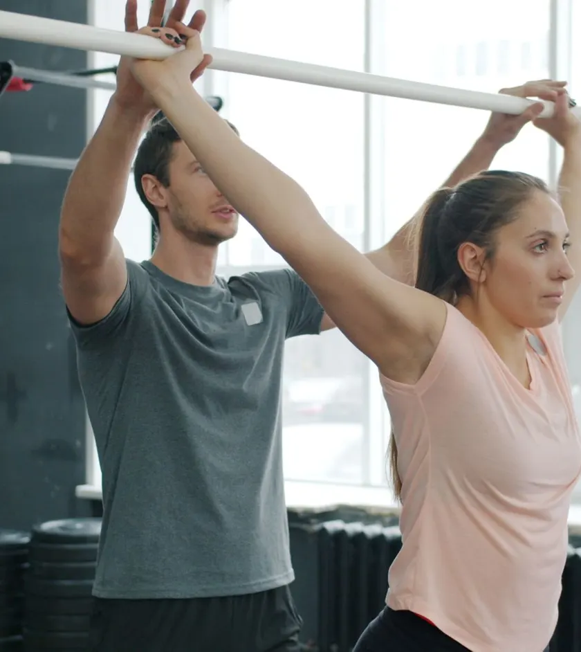 Trainer and client stretching with a bar in a fitness studio