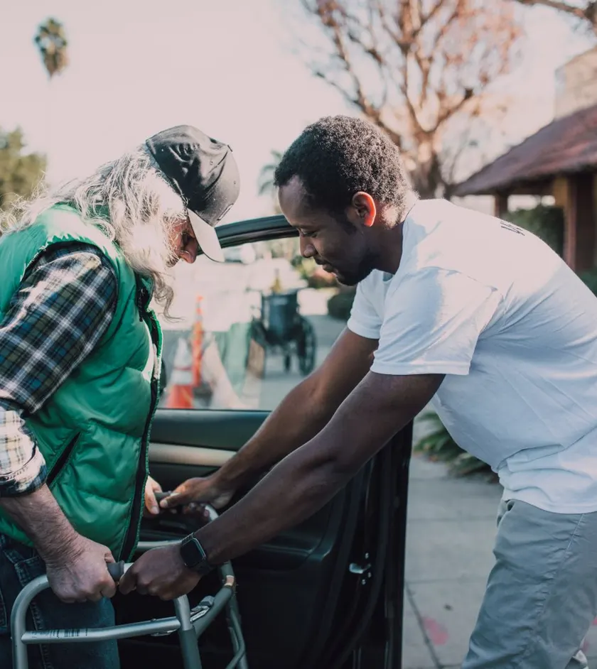 Caregiver helping a senior with a walker get into a car