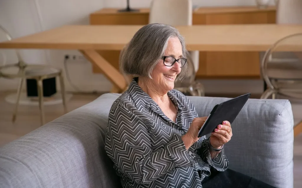 Senior woman smiling while using a tablet on a sofa