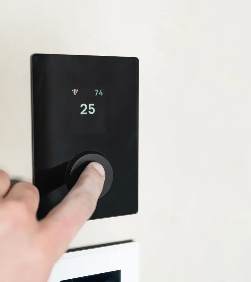Hand adjusting a modern smart thermostat on a wall