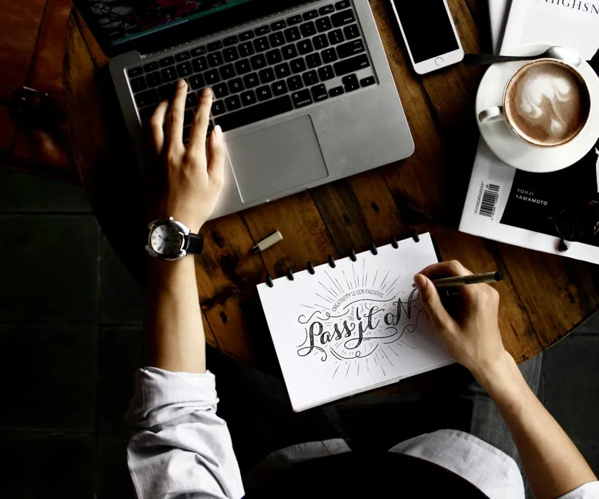 Designer sketching a website layout beside a laptop