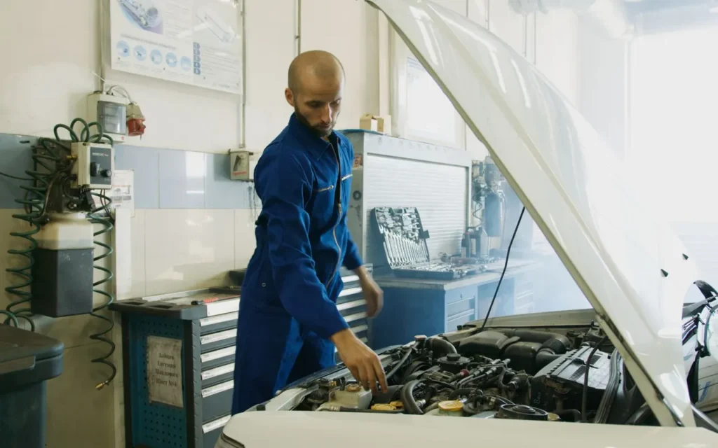 Mechanic inspecting a car engine under the hood in a garage