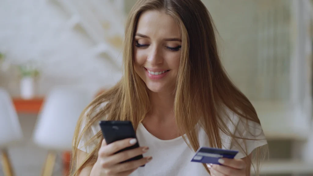 Customer smiling while holding a phone and credit card, ready to buy after clicking an ad