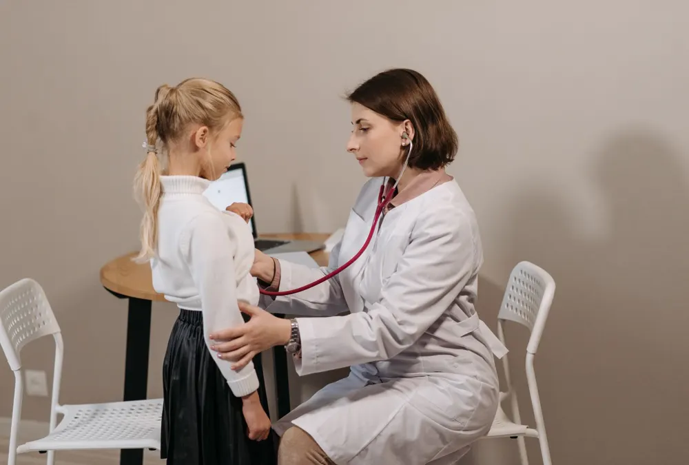 Pediatrician checking a girl’s lungs in an exam room